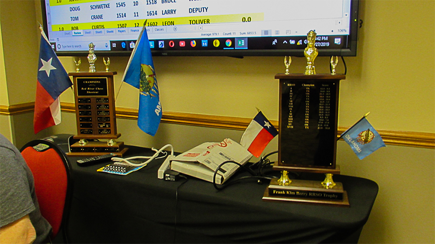 On the left is the original famous Traveling Trophy donated by the Wichita Falls Chess Club at RRSO II.  Little room remains for additional engraved plates.  This momento is safeguarded by the Tarrant County Chess Club year round.  On the right is the Frank Kim Berry RRSO Trophy which stays with the winning team.  The front plate has plenty of room for engraved scores extending well past 2027 (our Heritage year).  Photo by Mike Tubbs.